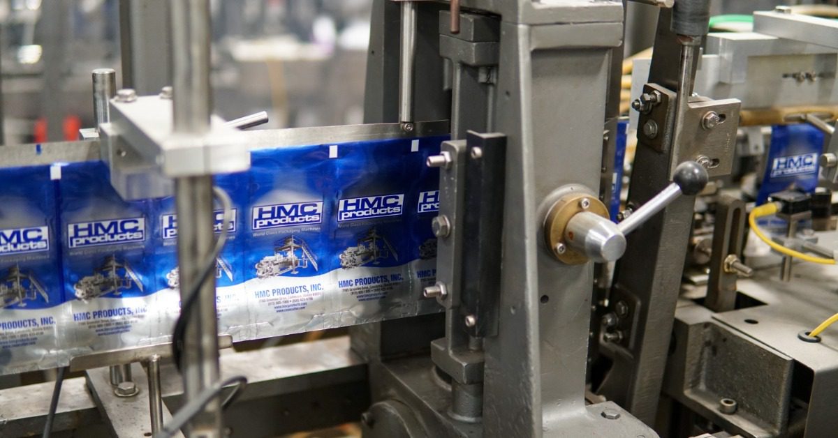 Sealed blue pouches moving along a narrow conveyor belt inside a blurred production area with metal equipment.