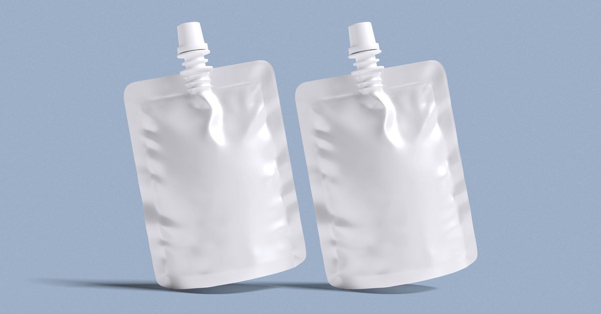 Two unlabeled pouch packages with spouts sit upright, casting a short shadow against a light blue background.