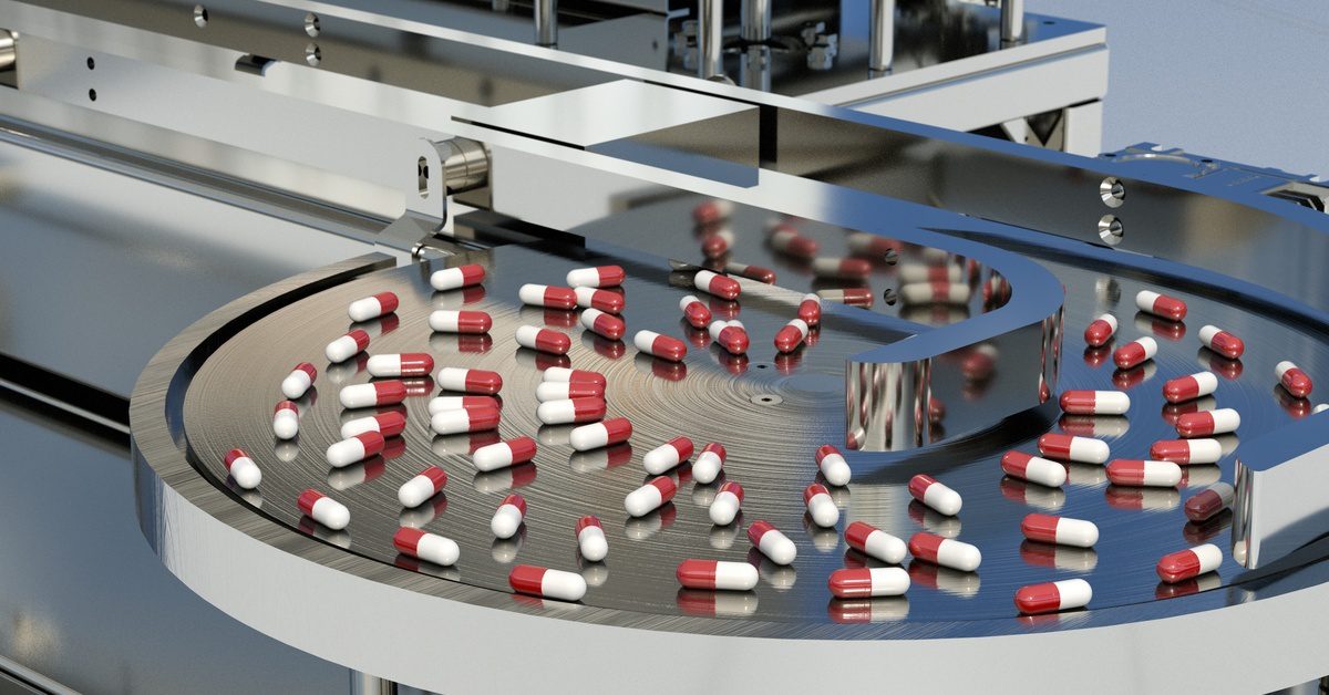 A variety of loose pills rest on the clean, circular metal surface of a large apparatus with multiple levels.