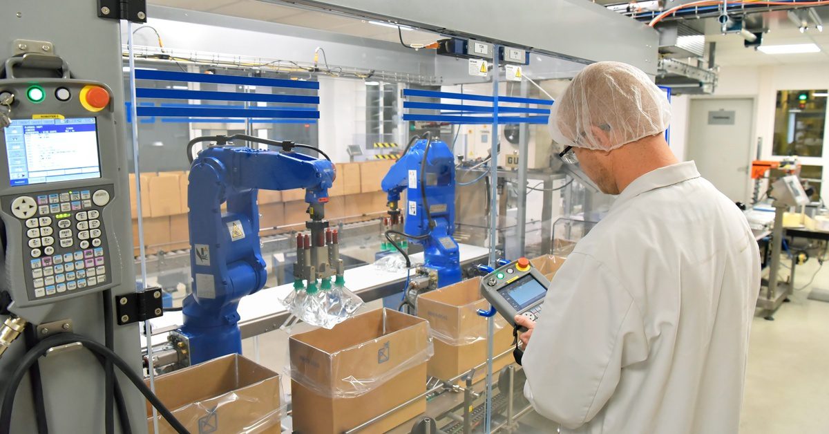 Automated bottling machinery with stainless steel, clear panels, and conveyor belts in a clean industrial facility.