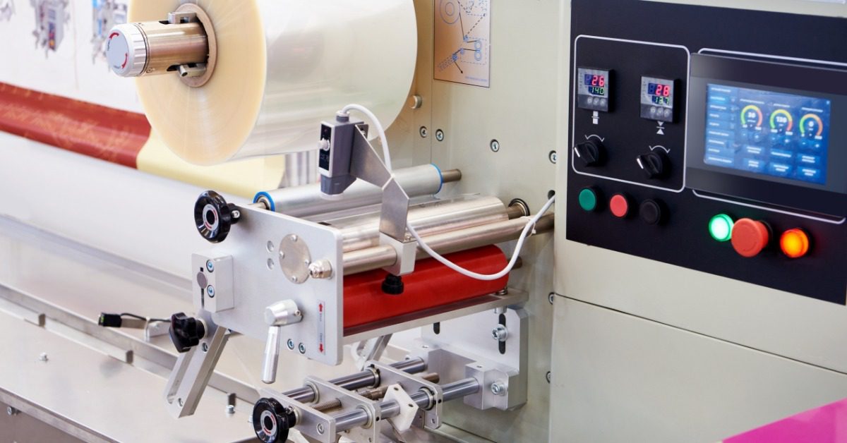 A horizontal packaging machine featuring a large roll of film and a control panel displaying the equipment's settings.