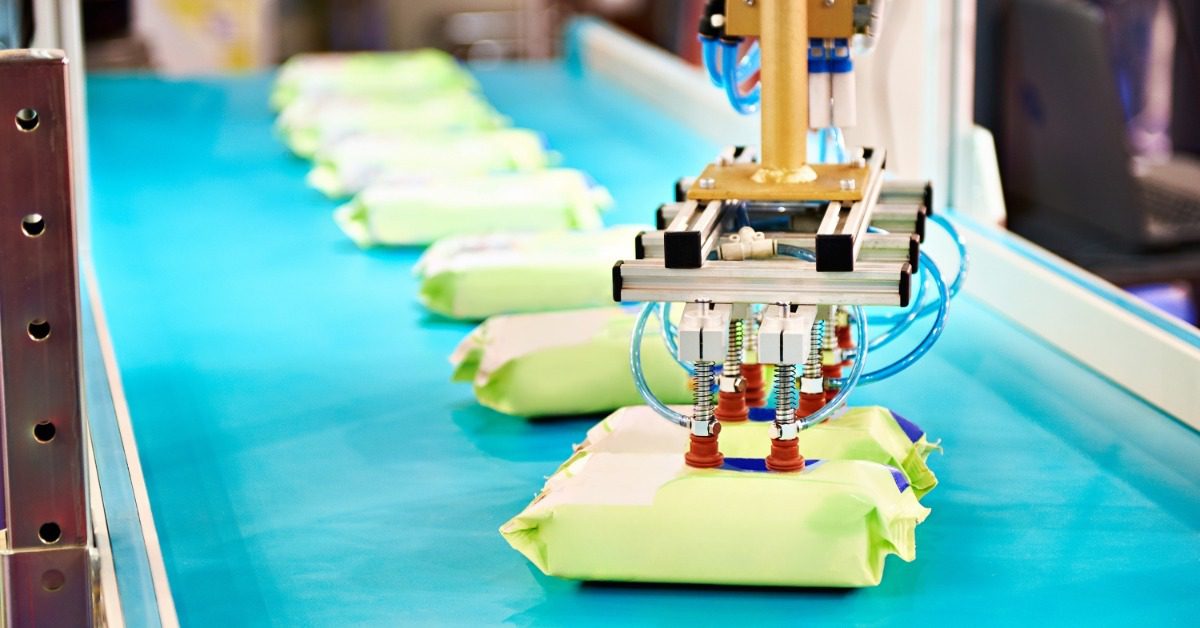 A robotic gripper reaches toward small plastic pouch packages on the conveyor belt of an automated packaging line.